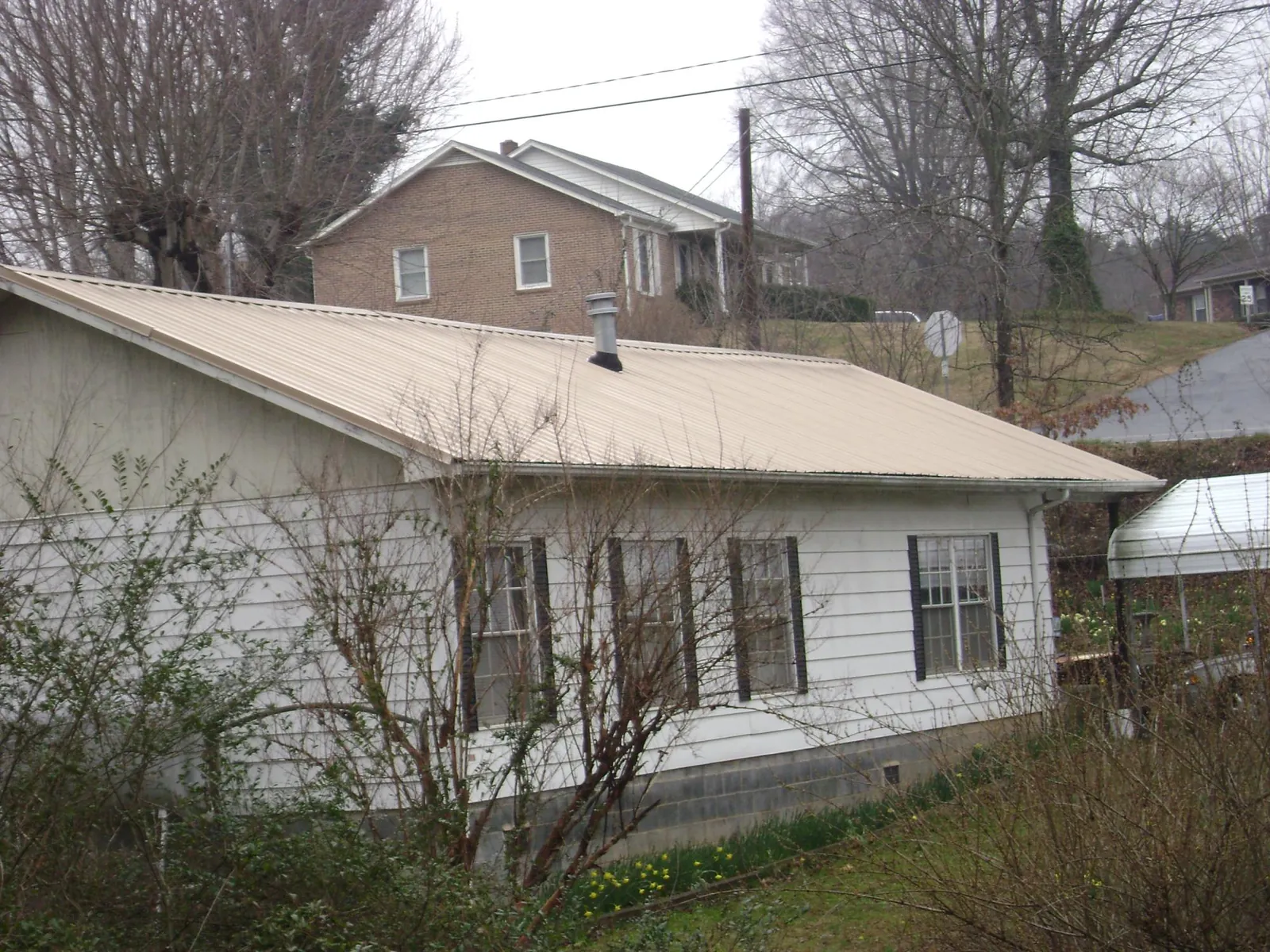 Tan metal roof on a white sided house set into a hillside — Commercial Roofing by Roofing Brothers in Burlington