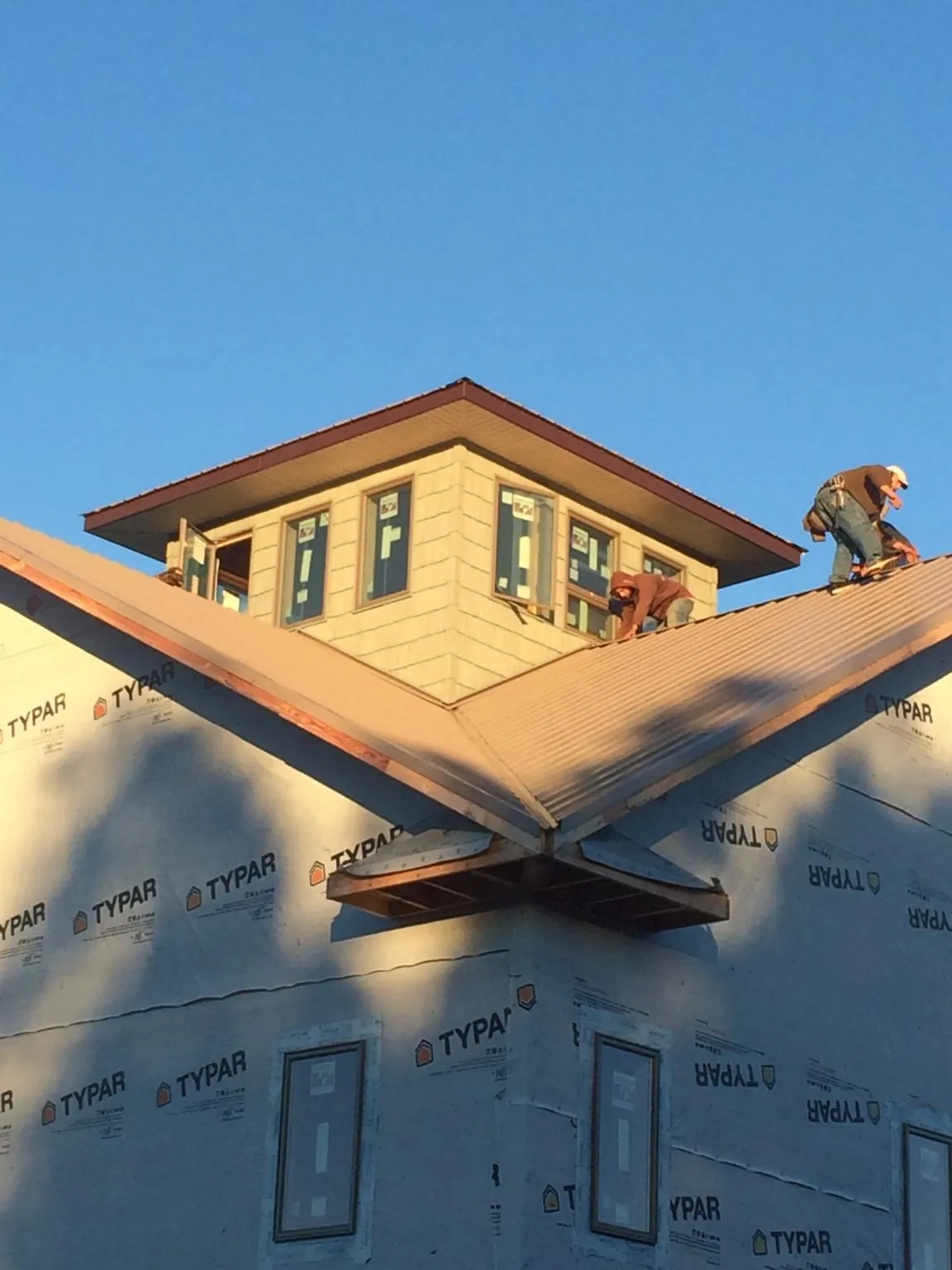 Roofers working around a rooftop cupola on a new metal roof at sunset — Roof Waterproofing in Burlington by Roofing Brothers